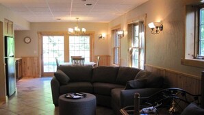 A spacious living room with a sectional sofa, a round ottoman, and a dining area with a table and chairs. - Perfect For Family Reunions/Weekend Getaways/Large Groups. A hidden oasis! (Fish Creek)