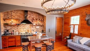 Una cocina rústica con pared de ladrillo, armarios de madera, una estufa grande y un colgador con lámpara.