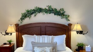 A neatly made bed with a wooden headboard, two bedside lamps, a decorative wall hanging, and a small table with a plant and a tissue box. - River View Place / beautiful view (Fries)