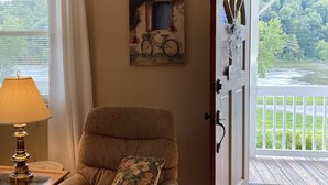 A cozy room with a brown armchair, a cushion, a lamp, and a painting of a bicycle. - River View Place / beautiful view (Fries)