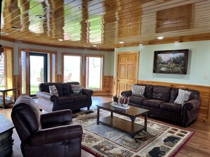 A cozy living room with two sofas, a coffee table, and a rug. There are large windows and a door leading outside.