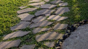 Un camino de piedra que lleva a un muelle junto al agua, con una silla y una sombrilla en el muelle.