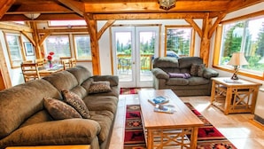 L’intérieur de ce chalet chaleureux est doté d’un grand canapé, d’un petit divan et d’une table en bois. De grandes fenêtres offrent une vue sur le paysage extérieur.