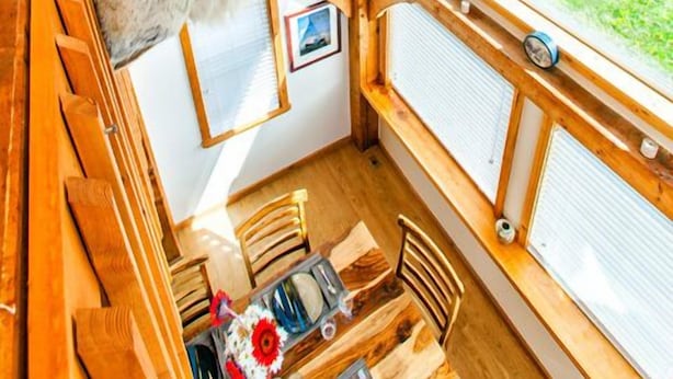 L’intérieur d’un chalet rustique, avec une tête de cerf accrochée au mur, des murs en bois et de grandes fenêtres donnant sur un paysage verdoyant.