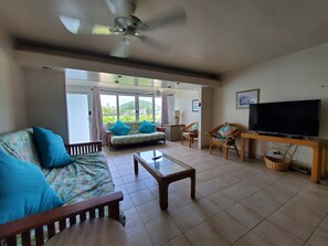 A spacious living room with a sofa, chairs, a coffee table, a television, and a ceiling fan.