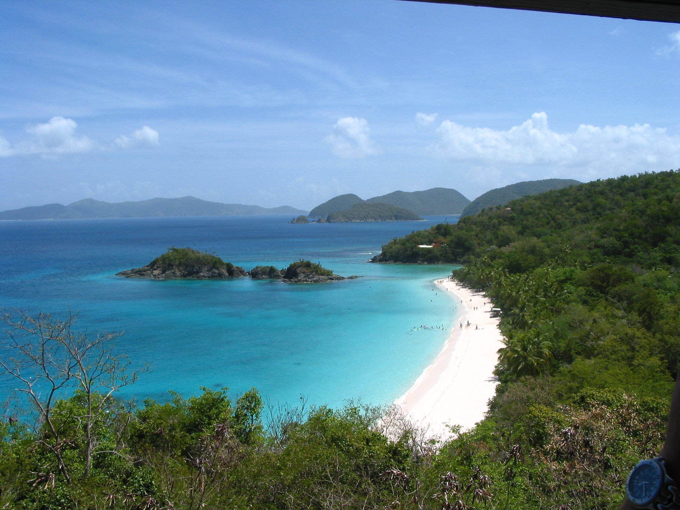 Ein Strand mit klarem türkisblauem Wasser, weißem Sand und üppiger Vegetation.