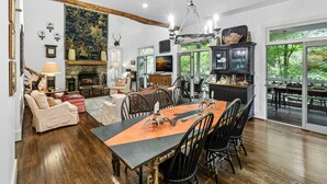 A spacious living area with a dining table, chairs, and a fireplace. There is a large window providing a view of the outdoors.