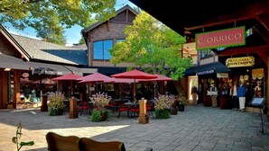 An outdoor café area with red umbrellas, wooden benches, and potted plants.