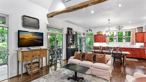 A spacious living room with a large TV, a sofa with patterned cushions, a coffee table, and a dining area with chairs.
