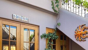 A building with a sign reading "Casa de Su Casa," a wooden bench, a potted plant, and a decorative sun sculpture.