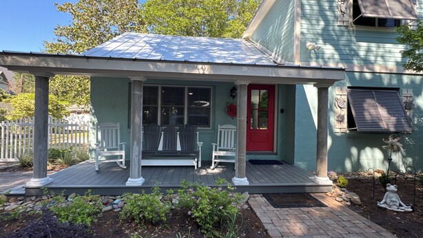 Une maison avec un porche, une porte rouge et un espace abrité avec des bancs.