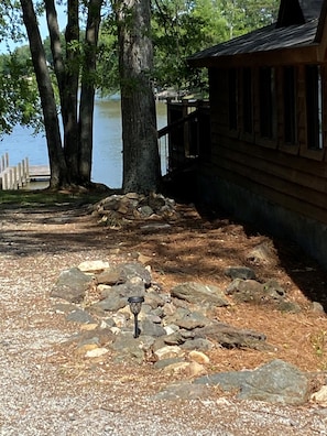En stuga vid en sjö med en grusgång, en stenmur och en träveranda.