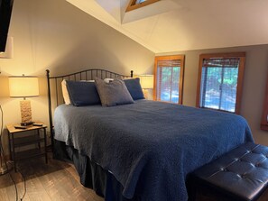 A bedroom with a bed, bedside lamps, a bench, and windows with blinds.