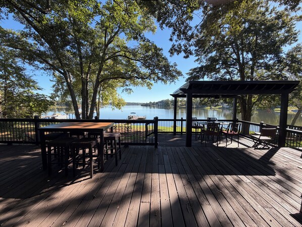A wooden deck with tables and chairs, overlooking a calm lake with boats.