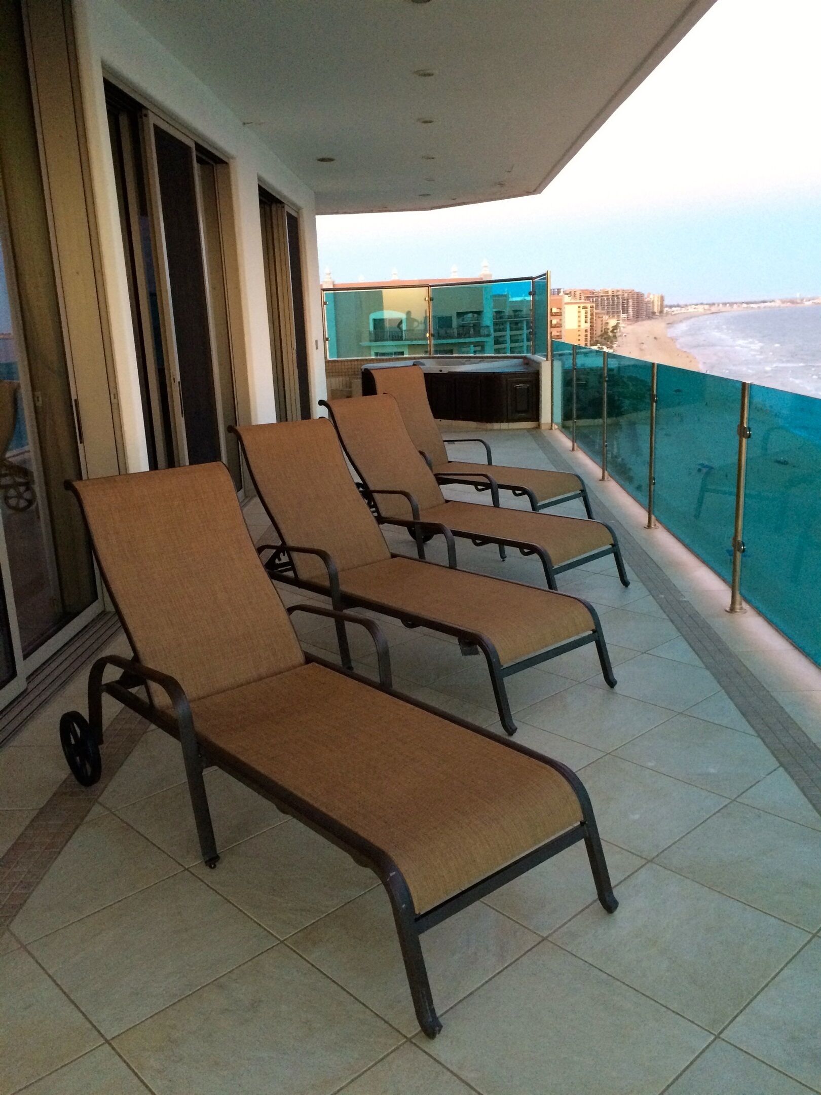 Een balkon met vier loungestoelen, een glazen balustrade en uitzicht op strand en zee.