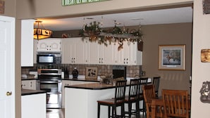 A kitchen with white cabinets, a central island, and a dining area with wooden chairs. - 2 Master Suites, Incredible Views Sleeps 10-12, Great Dock (Sunrise Beach)