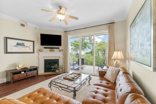 A spacious living room with a leather sofa, a glass coffee table, a fireplace, a television, and a balcony with outdoor furniture. - LUXURY CONDO W/ BEAUTIFUL GULF BEACH & REDFISH LAKE BALCONY VIEWS. 4 SWIM POOLS. (Santa Rosa Beach)