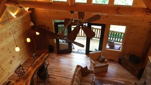 Un intérieur de cabine spacieux, avec un plancher en bois, un ventilateur de plafond, un canapé, une table basse et un coin repas comprenant une table et des chaises en bois.