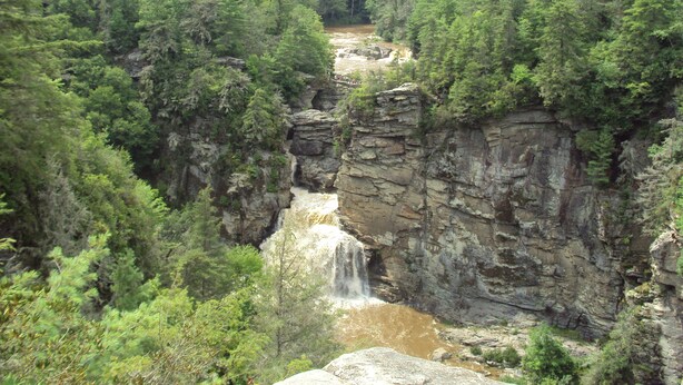 Un paysage naturel comprenant une cascade, une forêt dense et des falaises rocheuses.