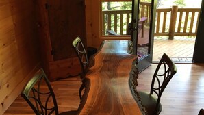 Une table à manger en bois, avec des chaises, une lampe et un meuble, dans une pièce aux murs en bois et offrant une vue sur l’extérieur.