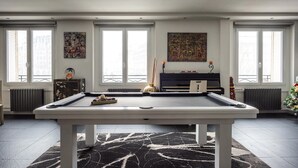 A pool table in a room with large windows, a piano, and decorative items. - Le Notre Dame – Luxury Duplex, Notre-Dame View, Left Bank (Paris)
