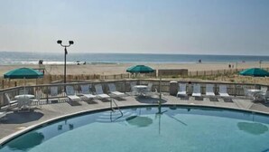 Zona de piscina con sillones de playa y sombrillas, con vistas a una playa.