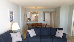 Una sala de estar con un sofá azul, una mesa de centro blanca y un comedor con una mesa y sillas de madera.