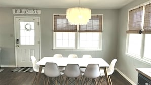 Comedor con una mesa y sillas blancas, una araña y una puerta con la leyenda 'BRIGANTINE'.