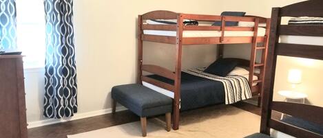 A bunk bed room with a desk and chair, a window with patterned curtains, and a ceiling fan.