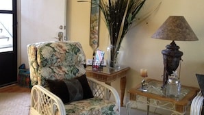 Ein Wohnzimmer mit einem blumigen Sessel, einem Beistelltisch mit Lampe, einem Spiegel und einer Pflanzvase.