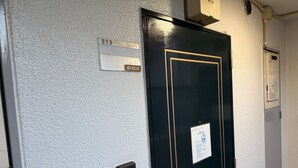 Eine schwarze Tür mit goldener Rahmung, einem Nummernschild, einem Rauchmelder und einem Aushang an der Wand.