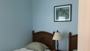 Une chambre avec deux lits simples, une table de chevet avec une lampe et un tableau encadré au mur.