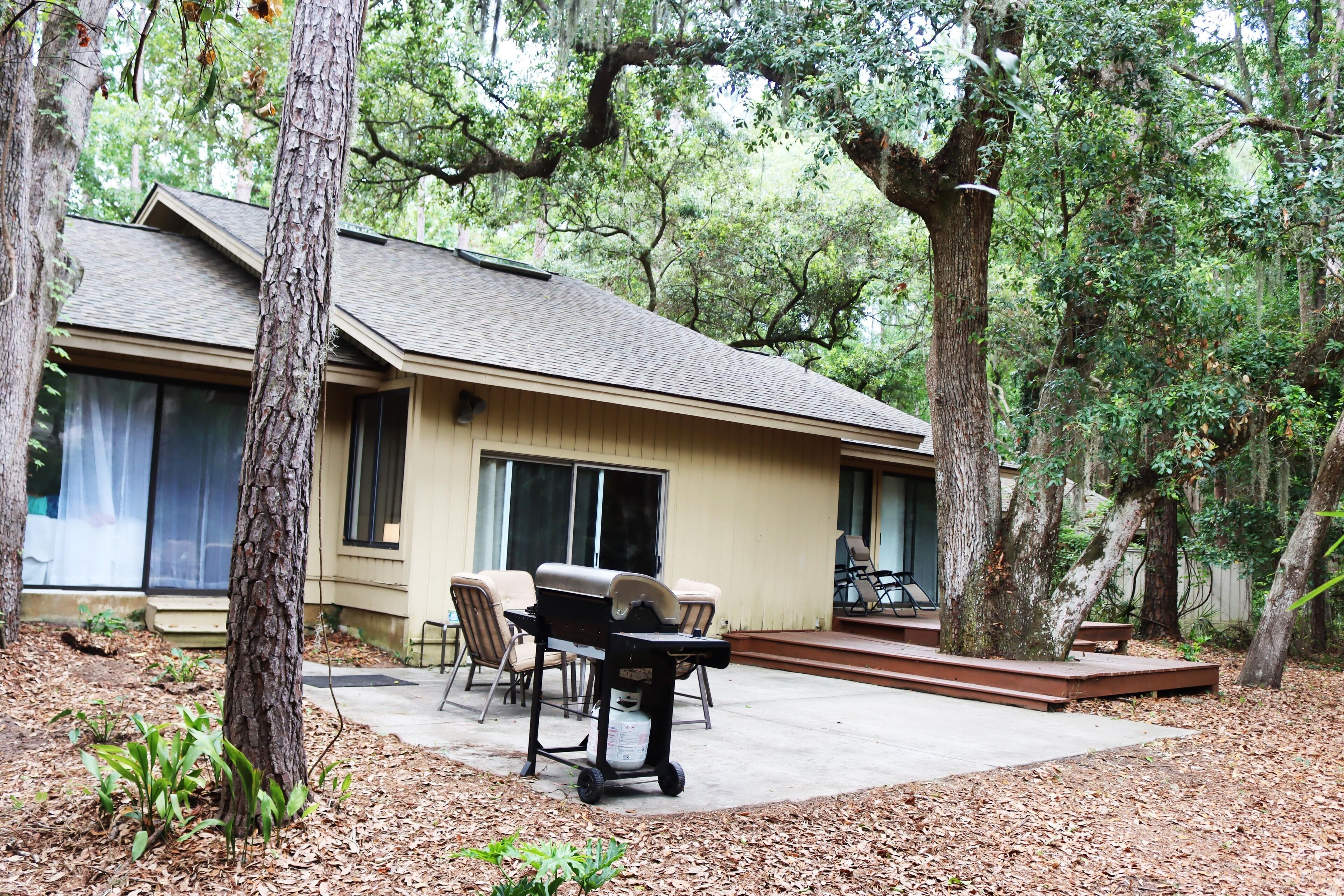 A house with a patio, outdoor furniture, and a large tree in the foreground.