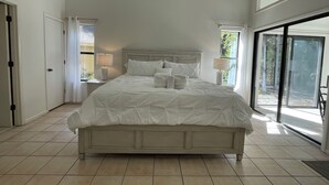 A spacious bedroom with a large bed, two bedside tables, and a view of the outdoors through a sliding glass door. - WOW! WHAT A DEAL for a HOUSE in SeaPines! Great Locations 2 BR -Pets ok (Hilton Head Island)