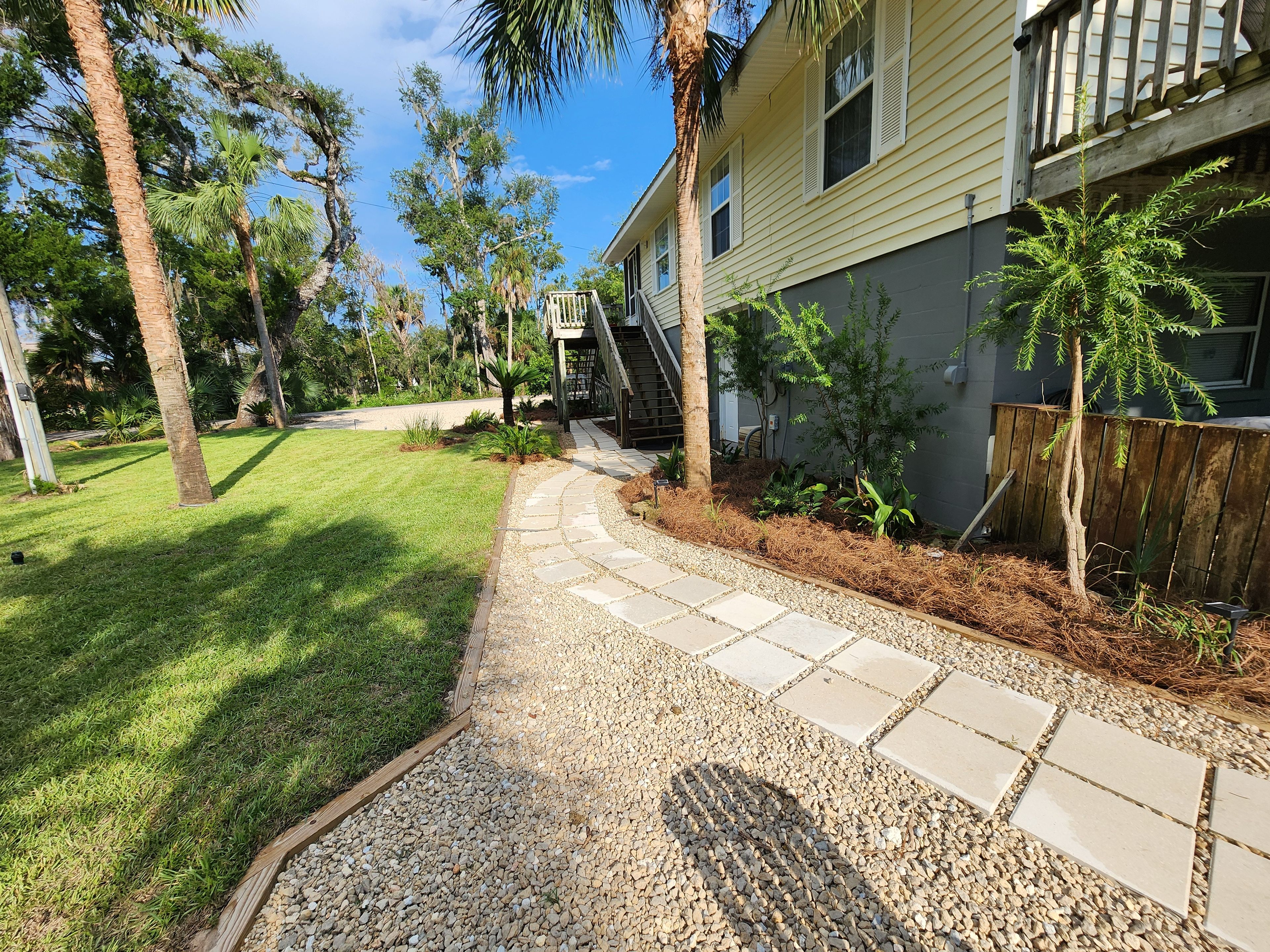 A pathway leading to a house with a wooden deck and a small garden area with various plants.