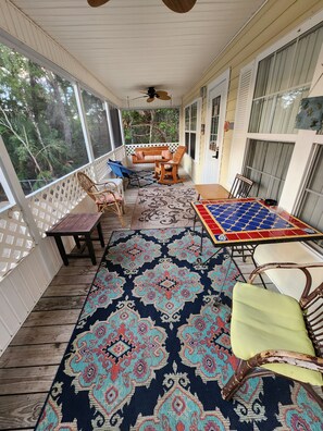 A covered porch with a wooden table, chairs, and a patterned rug.