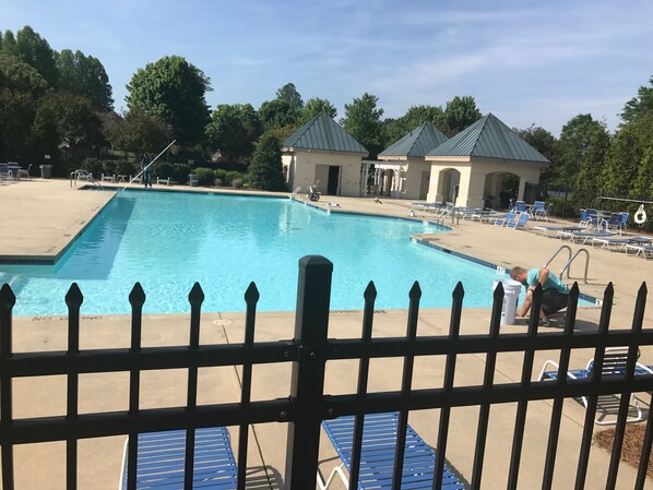 A swimming pool with a fenced area, lounge chairs, and a small building with a green roof.