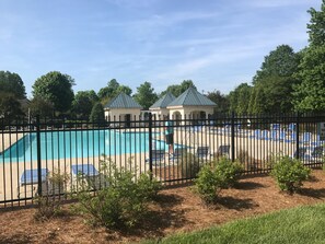 A swimming pool with lounge chairs and a fenced area, surrounded by trees and a small building with a green roof. - Lovely Home, Perfect location, Coliseum, Golf, HPU, Back Porch & Community pool (Jamestown)