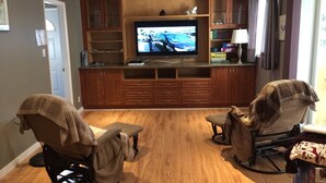 Un salon comprenant un meuble de rangement en bois pour l’équipement audiovisuel, un téléviseur et deux fauteuils inclinables.