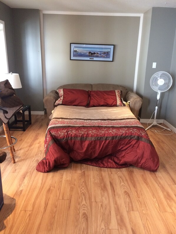 Quarto com cama, ventilador, quadro na parede e abajur em uma mesa lateral.