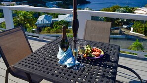 A balcony with a table set for two, featuring a bottle of champagne, two glasses, and a plate of vegetables. - Beautiful views, walk to Secret Harbour Beach (St. Thomas, VI)