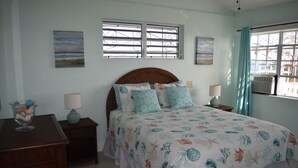 A bedroom with a large bed, a nightstand, a lamp, a decorative bowl, and a window with curtains. - Beautiful views, walk to Secret Harbour Beach (St. Thomas, VI)