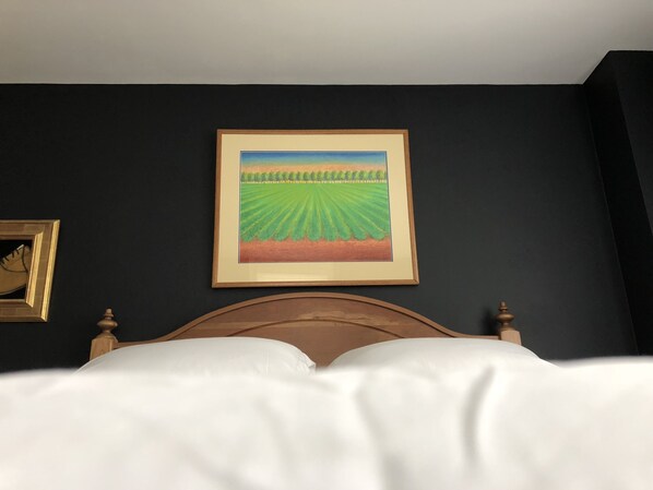A bedroom with a bed, a framed painting of a field, and a small golden-framed picture on the wall.