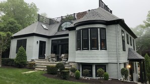 A two-story house with a curved corner design, a balcony, and a well-maintained garden.