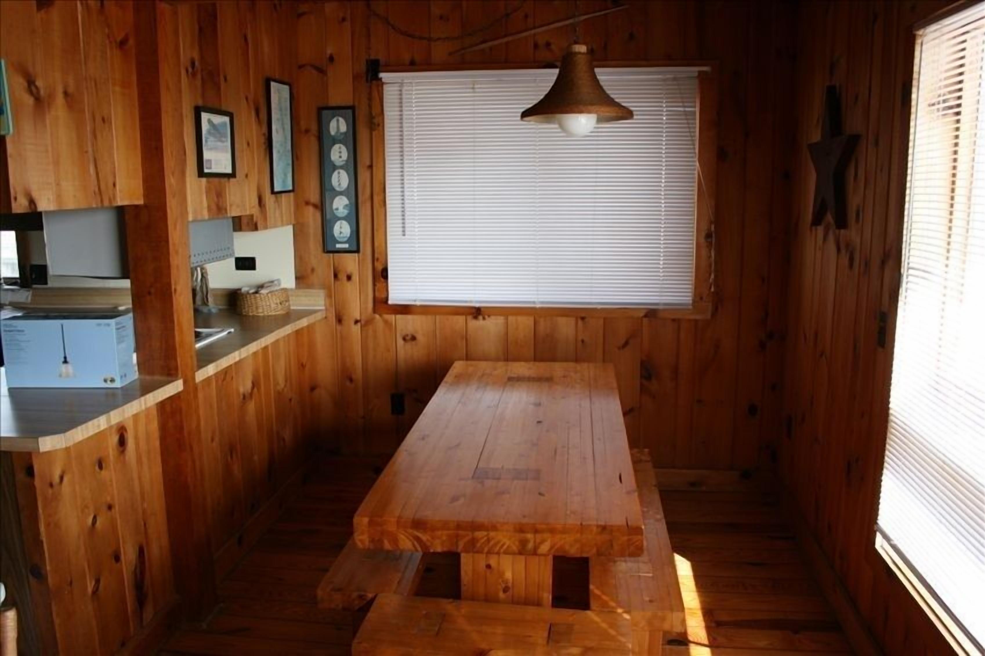 Un intérieur en bois comprenant un comptoir de cuisine, une table en bois et une fenêtre avec des stores.