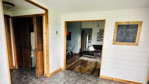 A spacious room with a tiled floor, a wooden door, and a chalkboard sign. - Relaxing Lakefront Cabin, Family + Lake + Dock + Sunset + Be Here, All Year Fun! (Watertown)