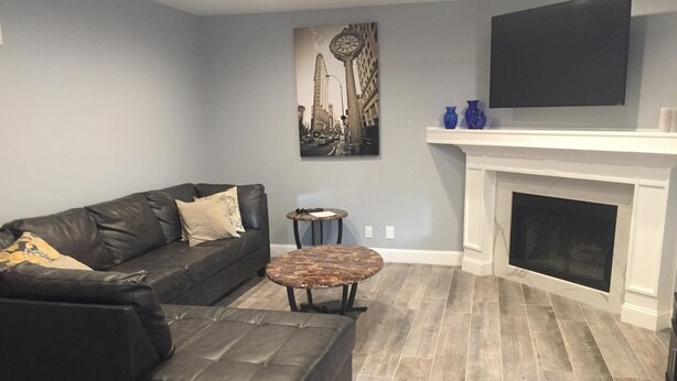 A living room with a black leather sofa, a round coffee table, a fireplace, and a cityscape painting on the wall.