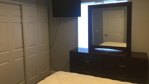 A bedroom with a bed, a dresser, a mirror, and a TV mounted on the wall.