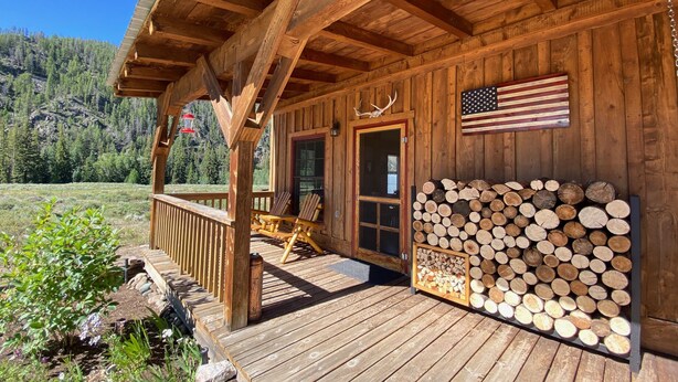 Een houten hut met een veranda, een stapel houtblokken en een Amerikaanse vlag.