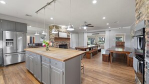 A spacious kitchen with a central island, grey cabinets, stainless steel appliances, and a brick accent wall. - The Gathering House: Fun outdoor nature vibes w pool 15 minutes to Waco, TX. (Crawford)